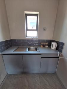 Una pequeña cocina con fregadero y ventana. en Eazy Rest, en Gqeberha