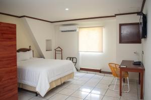 a bedroom with a bed and a desk and a window at Hotel Gardenia Inn in San Salvador