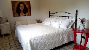 una camera da letto con un letto bianco con un dipinto sul muro di Carnaval Olinda-PE, casa à 5km do centro! a Olinda