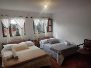 a bedroom with two beds and a chair and windows at Casa Alojamiento Maespit in Villa de Leyva +19 photos
