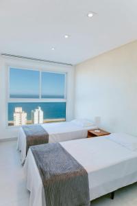 two beds in a room with a large window at Apto moderno c/ Vista Incrível para o Mar in Itaparica
