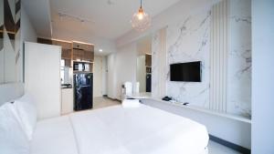 a white bedroom with a large bed and a refrigerator at Comfy Studio (No Kitchen) Apartment at Benson Supermall Mansion By Travelio in Surabaya +14 photos