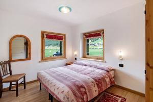 a bedroom with a bed and a chair and two windows at Appartamento Pizalegn Bait da Rez in Livigno