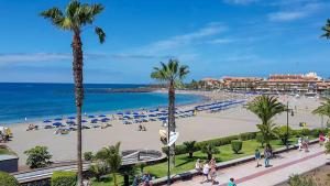 a beach with palm trees and chairs and the ocean at Las Vistas Cristianos by Welcome Tenerife in Los Cristianos