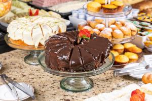 a chocolate cake on a table with other cakes and pastries at Park Tower Campinas Residence by Nacional Inn in Campinas