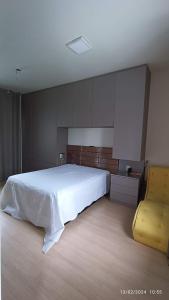 a bedroom with a white bed and a yellow chair at Quarto Belíssima in Pelotas