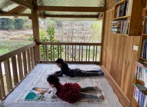 two girls laying on the floor in a room with books at Little House in KhauPha, Mu Cang Chai - homestay, cuisine, cafe in Mù Cang Chải