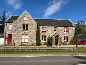a large brick house with a red door on a street at The Farmhouse Snug in Spean Bridge