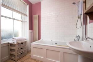a white bathroom with a tub and a sink at Pebble Cottage by Coast & Country Stays in Seahouses