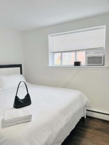 a black purse sitting on a white bed with a window at Elegant Brand New Apartment in Central Burlington in Burlington
