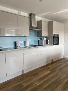 a kitchen with white cabinets and a wooden floor at Rooftops Apartment in Bletchley