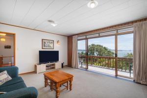 a living room with a tv and a large window at The Retreat - Front Beach Bach in Cooks Beach