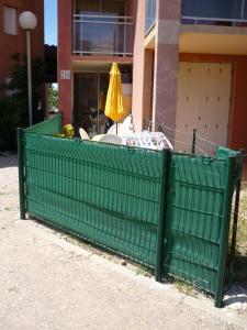 a green fence in front of a building with an umbrella at Barcarès F2 cabine, RDC, plage 50 m, 28 m2, 6 personnes in Le Barcarès
