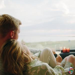 a couple sitting on a couch with a glass of wine at Tiny SeaSide - Loddenhøj in Aabenraa