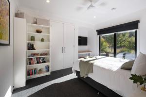 a white bedroom with a bed and a window at Cosy Edge- charming studio on edge of town in Daylesford