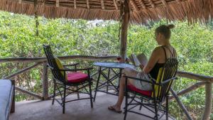 a woman sitting at a table reading a book at Stilts Diani Beach in Diani Beach