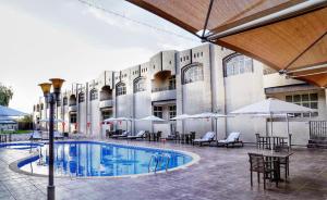 a hotel with a pool and tables and umbrellas at Asfar Resorts Al Ain in Al Ain