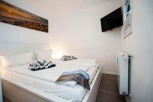 Cette chambre comprend un lit avec des draps blancs et une télévision à écran plat. dans l'établissement Strand Koje, à Westerland