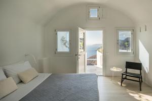 a white bedroom with a bed and a chair at Porto Fira Suites in Fira