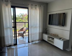 - un salon avec une télévision et une porte coulissante en verre dans l'établissement Apartamento Ju & Mar, à Itapoá