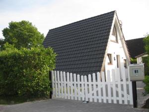 a white house with a black roof and a white fence at Ferienhaus Sylvia in Hoddersdeich