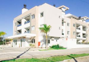 a white building with a palm tree in front of it at Modern apartment with barbecue CRR201 in Florianópolis