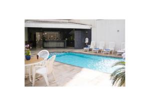a pool with white chairs and a table and a table and chairs at Mariano Palace Hotel in Campinas