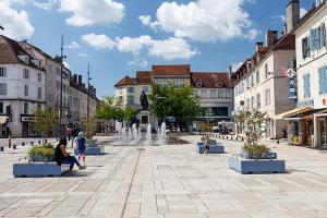 a woman sitting on a bench in a plaza with a fountain at Détente au Centre-Ville - Lons-le-Saunier in Lons-le-Saunier