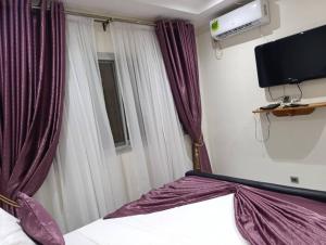 Schlafzimmer mit einem Bett mit lila Vorhängen und einem TV in der Unterkunft Résidence Angéline 4 studios in Yassa