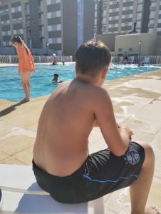a young boy sitting on a pole by a swimming pool at Apartamento completo , bem localizado in Pelotas