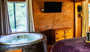 a large tub in a room with a window and a television at Chalé Jequitiba, hidro, lareira, natureza, Sul de Minas, Café da manhã in Sapucaí-Mirim