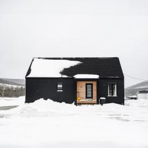 a small black house with snow on the roof at La Kobber Hüs - Élégance au coeur de la ville in Murdochville
