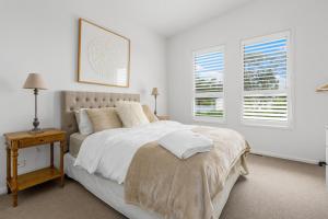 a white bedroom with a bed and two windows at Grandview on Bayview in Inverloch