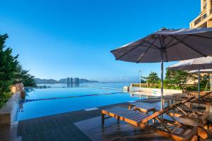 a swimming pool with chairs and an umbrella at Sanya Golden Phoenix Seaview Hotel in Sanya