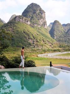 een man die naast een zwembad staat met bergen op de achtergrond bij Yangshuo One Thousand and One Courtyard Views B&B in Yangshuo