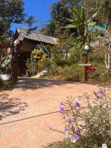 a garden with a building and some purple flowers at มาค่ะ ฟาร์มสเตย์ ห้วยเขย่ง สวนคุณตา สวนทุเรียนทองผาภูมิ in Ban Diso