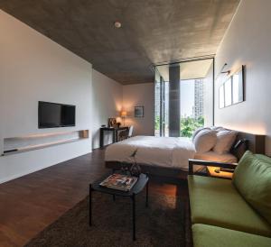 a bedroom with a bed and a couch and a tv at Norma Hotel Sathorn in Bangkok