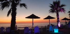 a sunset at the beach with palm trees and chairs and umbrellas at Casa da Cortiça in Seixal