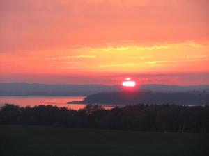 a sunset with the sun setting over the water at Ferienhaus "Cajo" am Malchiner See in Dahmen