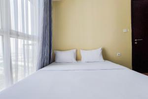 a bed with white pillows sitting next to a window at Strategic and Restful 1BR at Casa De Parco Apartment By Travelio in Tangerang +10 photos