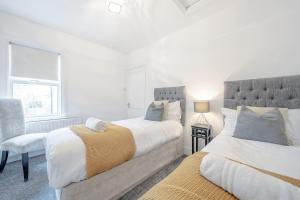 a white bedroom with two beds and a chair at New 3 Bed Victorian Dream House in Staines