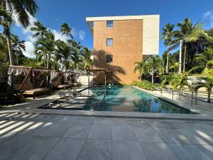 ein Swimmingpool vor einem Gebäude mit Palmen in der Unterkunft Amura Carneiros apartamento 3 quartos com piscina privativa in Praia dos Carneiros