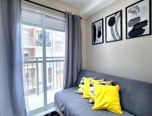 a couch with yellow pillows in a room with a window at Laguna 1212 - Moderno e Funcional in Sao Paulo