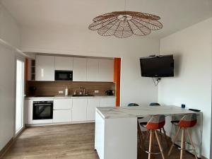 una cocina con armarios blancos y una isla de cocina con taburetes en Appartement « pépite » vue mer, en Saint-Cyprien 2 fotos más