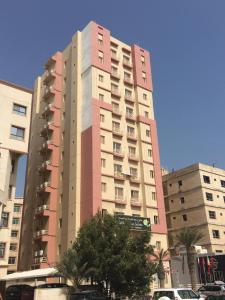 a tall pink building with cars parked in front of it at Pyramiza Hotel Al Mangaf فندق بيراميـــزا المنقف in Kuwait