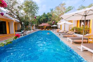 a pool with chairs and umbrellas next to a resort at Hoi An Phu Quoc Resort & Spa in Phu Quoc