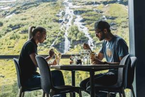two men sitting at a table eating food in front of a waterfall at Mountain apartment Røldal alpine center in Håra
