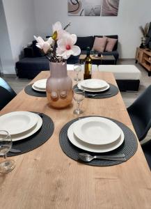 Una mesa de madera con platos y un jarrón con flores. en Melinta Stay - Near Airport, Rafina Port & Sea, en Artemida