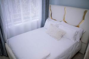 a white bed with white pillows and a window at Bellissima Homes in Kericho +3 photos