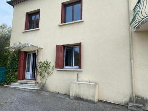 a white house with red windows and a plant at Appartement F3 de 60 m² au rez de chaussée d'une villa in Vézénobres
